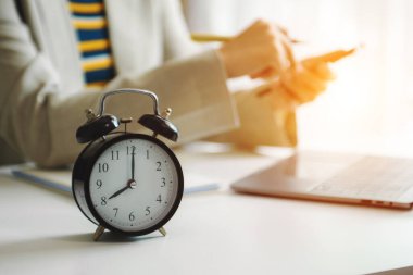 Masadaki çalar saat. Modern ofis binasında çalışan akıllı telefon, dizüstü bilgisayar ve tablet kullanan iş adamları 