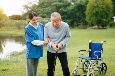 Asyalı genç bakıcı hemşire yaşlı bir erkeğin dışarıda yürümesini destekliyor. Uzman doktorlar yaşlı yetişkinlere yardım eder ve onlarla ilgilenir. Huzurevi hastane bahçesi konsepti