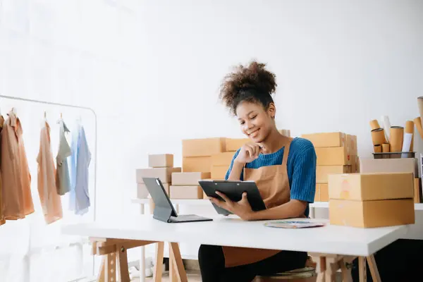 Akıllı telefon tutan genç bir kadın, ödeme başarısını gösteren bir tablet ve sarı paket kutusu olan kredi kartını ofiste online alışveriş kavramı olarak gösteriyor.