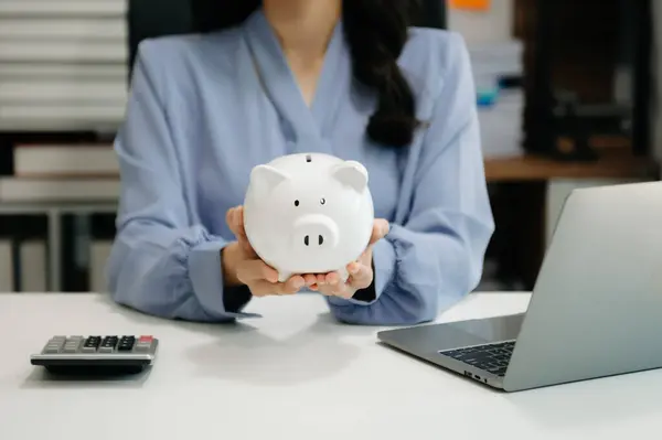 Kadın domuz kumbarasıyla bozuk para veriyor. iş finans tasarrufu ve yatırım konsepti. ev ofisinde.
