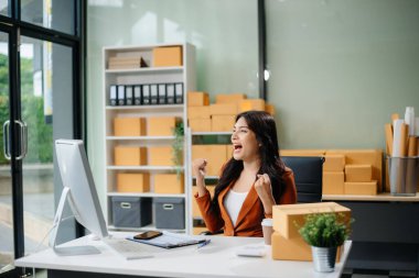 Startup small business SME, Entrepreneur owner woman using smartphone or tablet taking receive and checking online purchase shopping order to preparing pack product box.