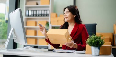 Startup small business SME, Entrepreneur owner woman using smartphone or tablet taking receive and checking online purchase shopping order to preparing pack product box.