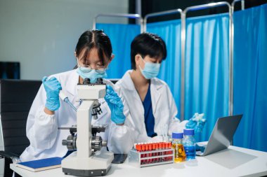 Healthcare professionals in a lab analyze virus models using a tablet and microscope. Medical research, biotechnology, and lab testing for scientific study and virus research