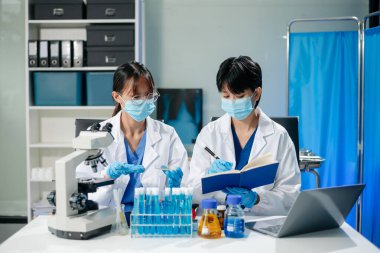 Healthcare professionals in a lab analyze virus models using a tablet and microscope. Medical research, biotechnology, and lab testing for scientific study and virus research