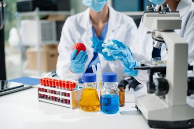 Healthcare professionals in a lab analyze virus models using a tablet and microscope. Medical research, biotechnology, and lab testing for scientific study and virus research