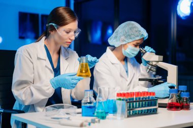 Bir tıp laboratuvarında araştırma yapan genç bilim adamları, ön plandaki bir araştırmacı, tıp laboratuarında bir mikroskop kullanıyor..  