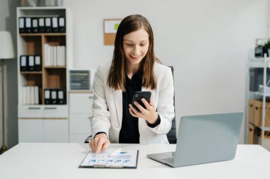 Kendine güvenen iş uzmanı, gülümseyen, dizüstü bilgisayarda yazan ve dijital tableti yaratıcı ofiste tutan çekici genç bir kadın.