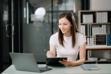 Güzel bir kadın çalışma yerinde otururken dizüstü bilgisayar ve tablet kullanıyor. İşine odaklan.