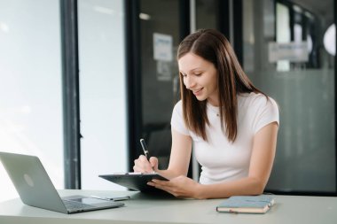 Güzel bir kadın çalışma yerinde otururken dizüstü bilgisayar ve tablet kullanıyor. İşine odaklan.