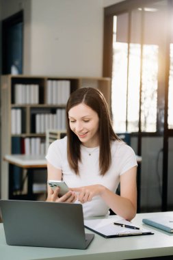 Güzel bir kadın çalışma yerinde otururken dizüstü bilgisayar ve tablet kullanıyor. İşine odaklan.