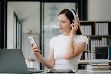 Üniversite kütüphanesinde okuyan, bilgisayarını, tabletini ve kulaklığını kullanan, video sohbeti yapan çekici, mutlu genç bir öğrenci..