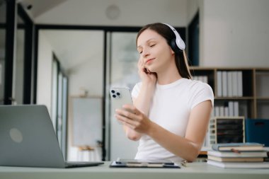 Üniversite kütüphanesinde okuyan, bilgisayarını, tabletini ve kulaklığını kullanan, video sohbeti yapan çekici, mutlu genç bir öğrenci..