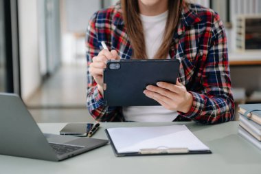 Güzel bir kadın çalışma yerinde otururken dizüstü bilgisayar ve tablet kullanıyor. İşine odaklan.