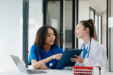  Doktor, profesyonel baş hemşire ya da cerrahla konuşuyor. Dijital tablet bilgisayar kullanıyorlar. Muhtelif sağlık uzmanları test sonuçlarını hastanede masasında tartışıyor. 