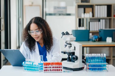 Bir tıp laboratuvarında araştırma yapan genç bilim adamları, ön plandaki bir araştırmacı, tıp laboratuarında bir mikroskop kullanıyor..  