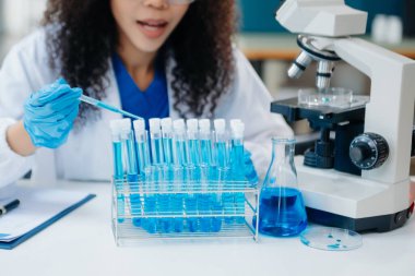 Bir tıp laboratuvarında araştırma yapan genç bilim adamları, ön plandaki bir araştırmacı, tıp laboratuarında bir mikroskop kullanıyor..  