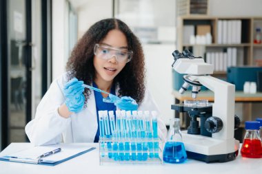 Bir tıp laboratuvarında araştırma yapan genç bilim adamları, ön plandaki bir araştırmacı, tıp laboratuarında bir mikroskop kullanıyor..  