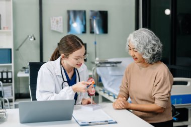 Doctor in white suit take notes while discussing and Asian elderly, man patient who lying on bed with receiving saline solution in hospital or clinic