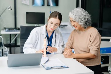 Doctor in white suit take notes while discussing and Asian elderly, man patient who lying on bed with receiving saline solution in hospital or clinic