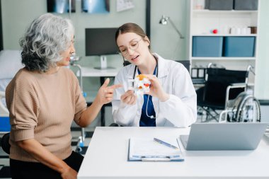 Doctor in white suit take notes while discussing and Asian elderly, man patient who lying on bed with receiving saline solution in hospital or clinic
