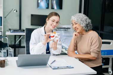 Doctor in white suit take notes while discussing and Asian elderly, man patient who lying on bed with receiving saline solution in hospital or clinic