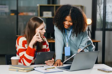 İki iş adamı akıllı telefondan konuşuyor ve ofiste dizüstü bilgisayar kullanıyorlar..