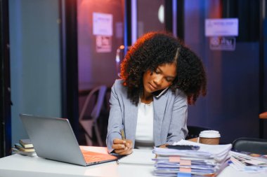 Afrikalı kadın migren ağrısı çekiyor. Ofiste dizüstü bilgisayar ve tablet üzerinde çalışırken aşırı çalışan iş kadını finansör.