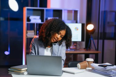 Afrikalı kadın migren ağrısı çekiyor. Ofiste dizüstü bilgisayar ve tablet üzerinde çalışırken aşırı çalışan iş kadını finansör.