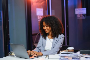 Afrikalı kadın migren ağrısı çekiyor. Ofiste dizüstü bilgisayar ve tablet üzerinde çalışırken aşırı çalışan iş kadını finansör.