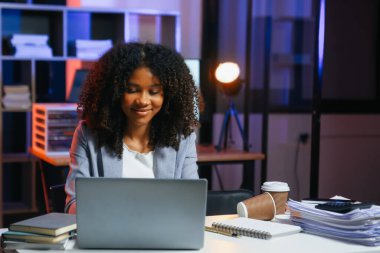 Afrikalı kadın migren ağrısı çekiyor. Ofiste dizüstü bilgisayar ve tablet üzerinde çalışırken aşırı çalışan iş kadını finansör.