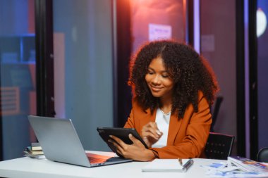 Afrikalı kadın migren ağrısı çekiyor. Ofiste dizüstü bilgisayar ve tablet üzerinde çalışırken aşırı çalışan iş kadını finansör.
