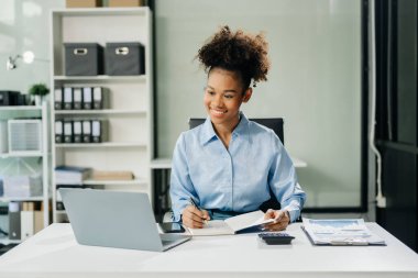 Kendine güvenen iş uzmanı, gülümseyen, dizüstü bilgisayarda yazan ve dijital tableti yaratıcı ofiste tutan çekici genç bir kadın..