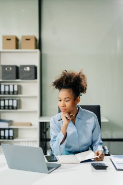 Kendine güvenen iş uzmanı, gülümseyen, dizüstü bilgisayarda yazan ve dijital tableti yaratıcı ofiste tutan çekici genç bir kadın..