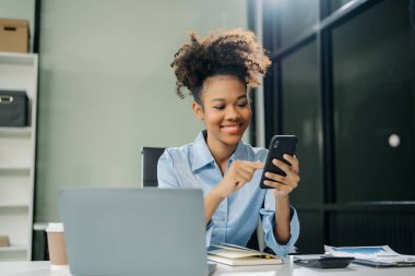 Kendine güvenen iş uzmanı, gülümseyen, dizüstü bilgisayarda yazan ve dijital tableti yaratıcı ofiste tutan çekici genç bir kadın..