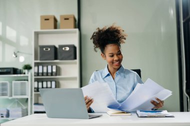 Kendine güvenen iş uzmanı, gülümseyen, dizüstü bilgisayarda yazan ve dijital tableti yaratıcı ofiste tutan çekici genç bir kadın..