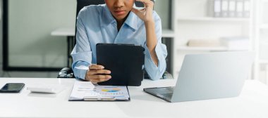 Kendine güvenen iş uzmanı, gülümseyen, dizüstü bilgisayarda yazan ve dijital tableti yaratıcı ofiste tutan çekici genç bir kadın..