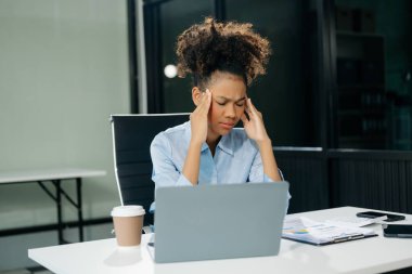 Woman feeling migraine head strain.Overworked businesswoman financier while working on laptop and tablet at office.