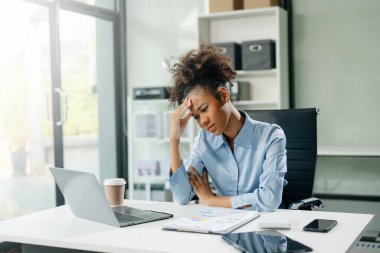 Woman feeling migraine head strain.Overworked businesswoman financier while working on laptop and tablet at office.