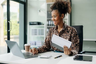 Kendine güvenen iş uzmanı, gülümseyen, dizüstü bilgisayarda yazan ve dijital tableti yaratıcı ofiste tutan çekici genç bir kadın..