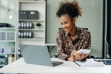 Kendine güvenen iş uzmanı, gülümseyen, dizüstü bilgisayarda yazan ve dijital tableti yaratıcı ofiste tutan çekici genç bir kadın..