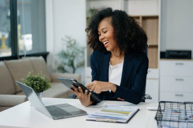 Modern ofiste elinde not defteri ve tabletle gülümseyen kendine güvenen bir kadın.
