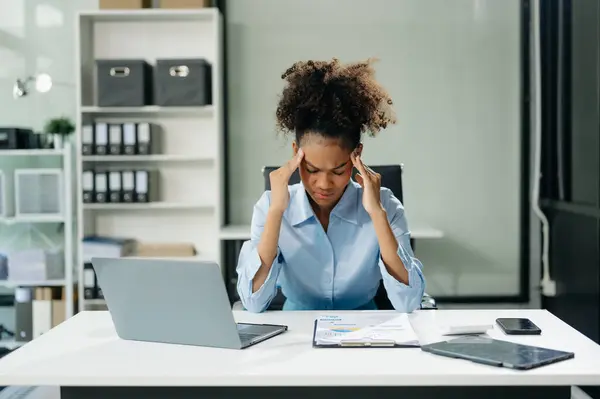 Woman feeling migraine head strain.Overworked businesswoman financier while working on laptop and tablet at office.