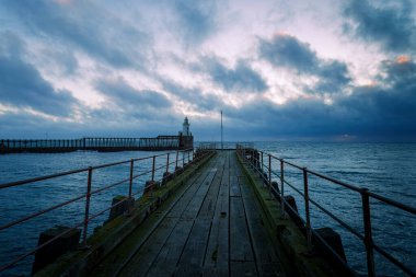 Arka planda günbatımı olan iskelede deniz feneri