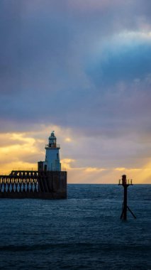Gün batımında sahilde bir deniz fenerinin dikey görüntüsü.