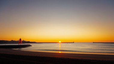 South Shields limanında gün doğumu, kuzey ve güney rıhtımlarında güneş doğuyor, yumuşak dalgalar üzerinde sarı bir parıltı yayıyor, Temmuz 2025