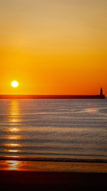 South Shields limanında gün doğumu, kuzey ve güney rıhtımlarında güneş doğuyor, yumuşak dalgalar üzerinde sarı bir parıltı yayıyor, Temmuz 2025