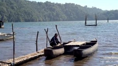 Buleleng, Bali, Endonezya 23 Ekim 2024: Yabancı turistler Tamblingan Gölü 'ndeki yerel bir kayıkçının rehberliğinde geleneksel bir kanoda oturuyorlar ve bu volkanik gölün sakin manzarasının tadını çıkarıyorlar..