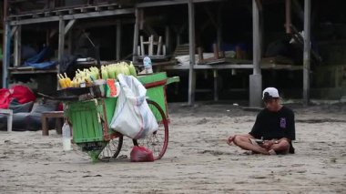 Bali, Endonezya, 18 AĞUSTOS 2023-A plajda portatif bir ızgarayla oturmuş, sıcak gün ışığında rahat bir sahil manzarasında yerel bir sokak yemeği sahnesini yakalıyor..