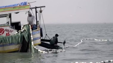 Jakarta Körfezi, Endonezya DEC 24, 2023: Bir balıkçı günün erken saatlerinde açık denizde bir balıkçı ağı çekiyor, parlak tropikal güneş ışığı altında geleneksel balıkçılık uygulamalarını yakalıyor.