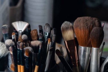 Yumuşak ışıklandırmalı ve koyu arkaplanlı kaplarda düzenli olarak düzenlenmiş çeşitli profesyonel makyaj fırçalarının yakın çekimi, dokusu ve ayrıntısı vurgulanıyor.